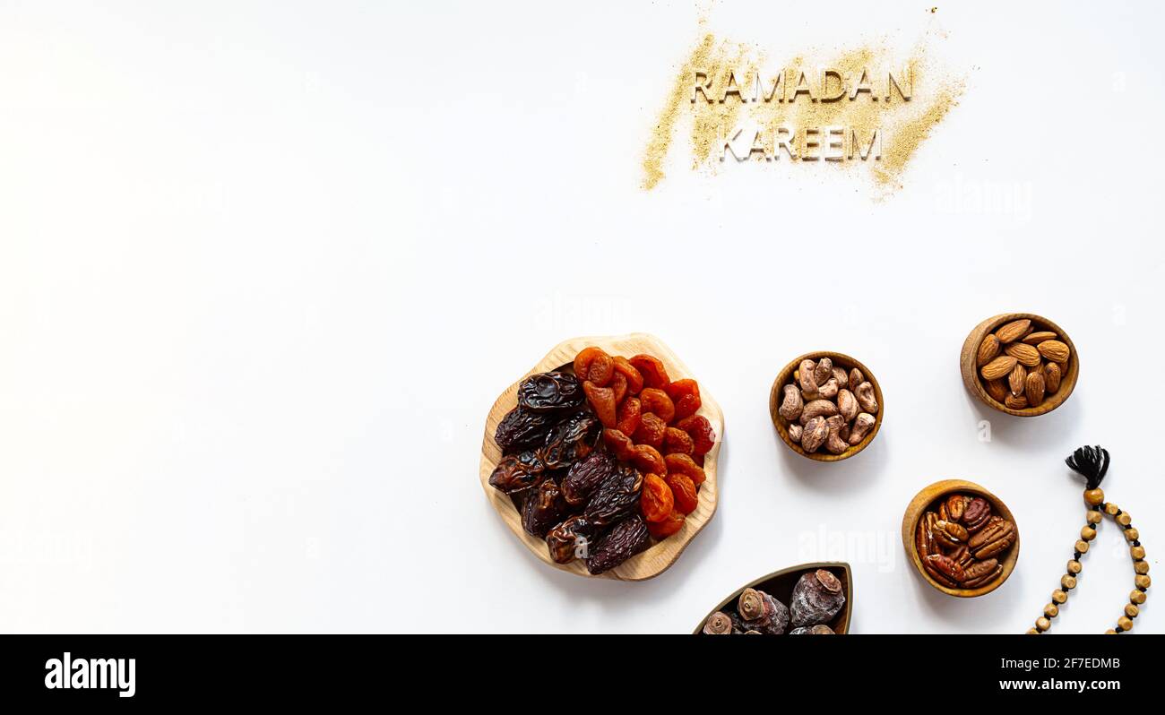 'Ramadan Kareem' and muslim Iftar food, modern festive concept in gold and white colors. Ramadan Kareem with premium dates, nuts, dried fruits in wood Stock Photo
