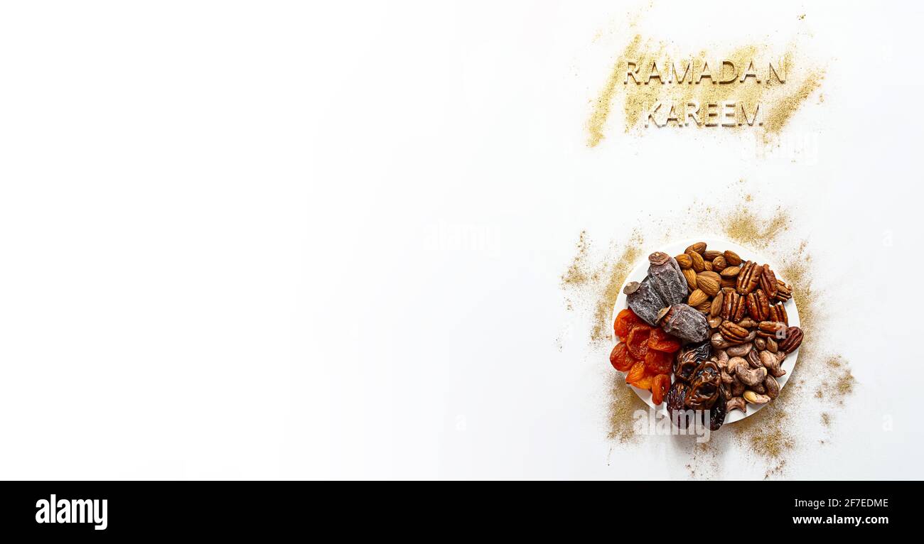 'Ramadan Kareem' and Iftar food, modern festive concept in gold and white colors. Muslim Ramazan Kareem with premium dates, nuts, dried fruits. Stock Photo