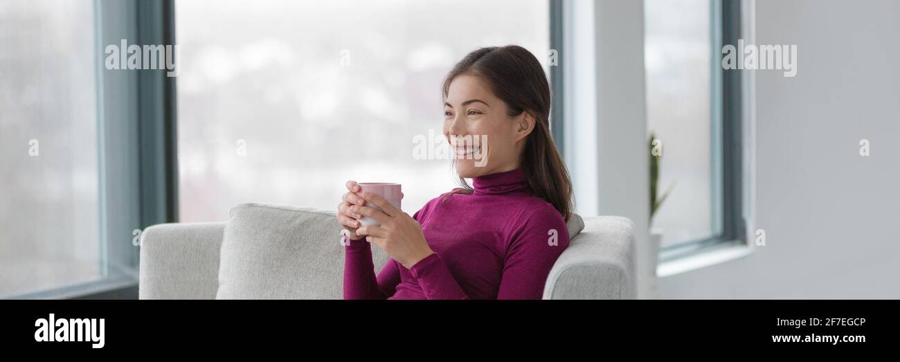 Happy Asian woman relaxing drinking coffee cup sitting in comfortable living room. Panoramic banner Luxury Home lifestyle. Stock Photo