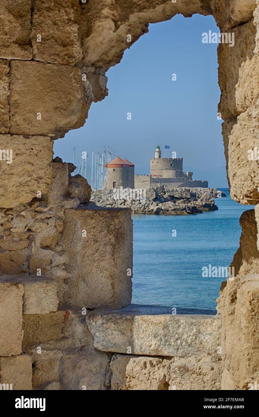 Beautiful view from the embrasure of the fortress wall on the medieval fort and windmills on the coast (Rhodes, Greece) Stock Photo