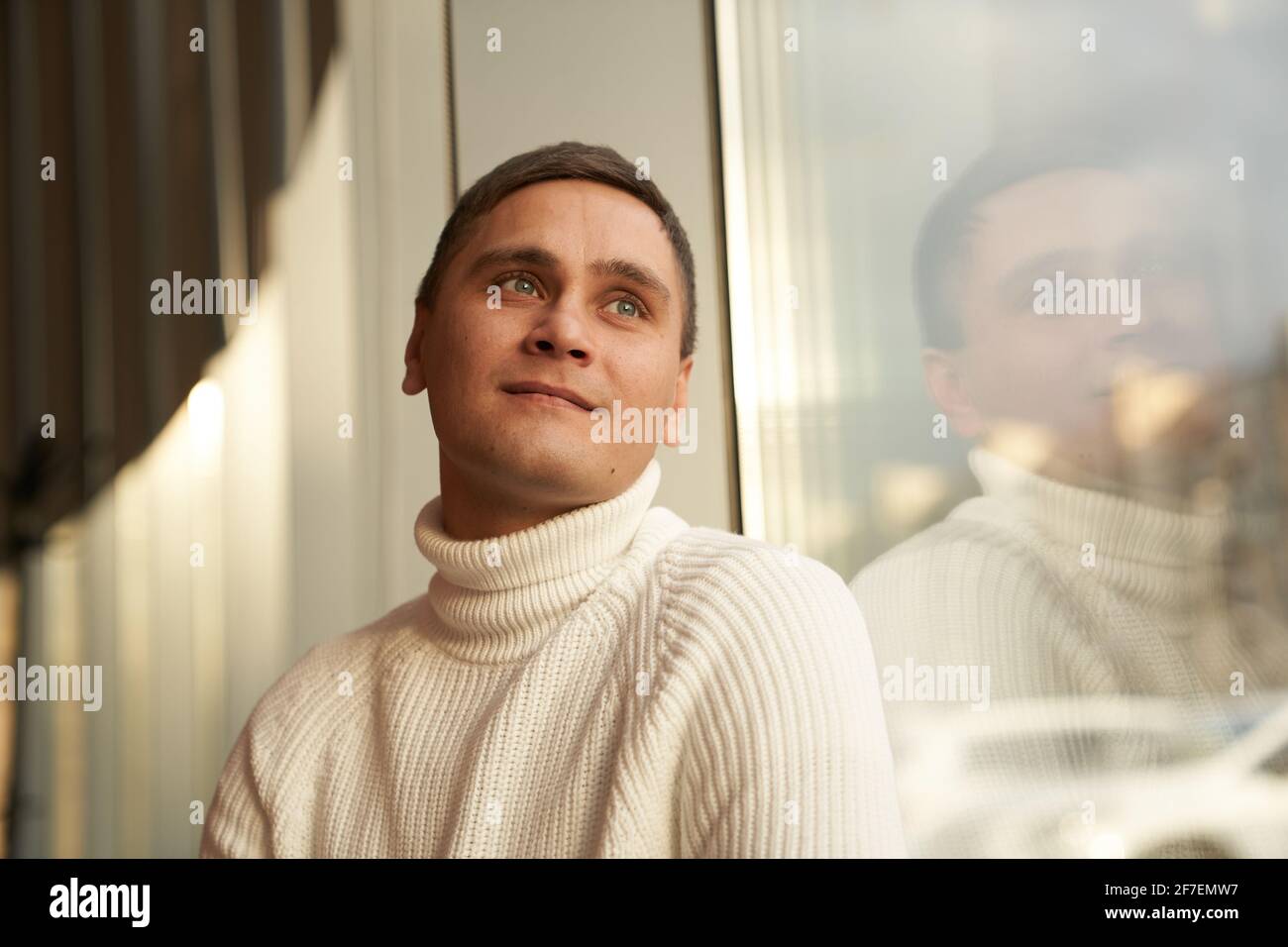 The handsome man in the room smiles and looks into the distance. A man in a white sweater. Copy space. High quality photo Stock Photo