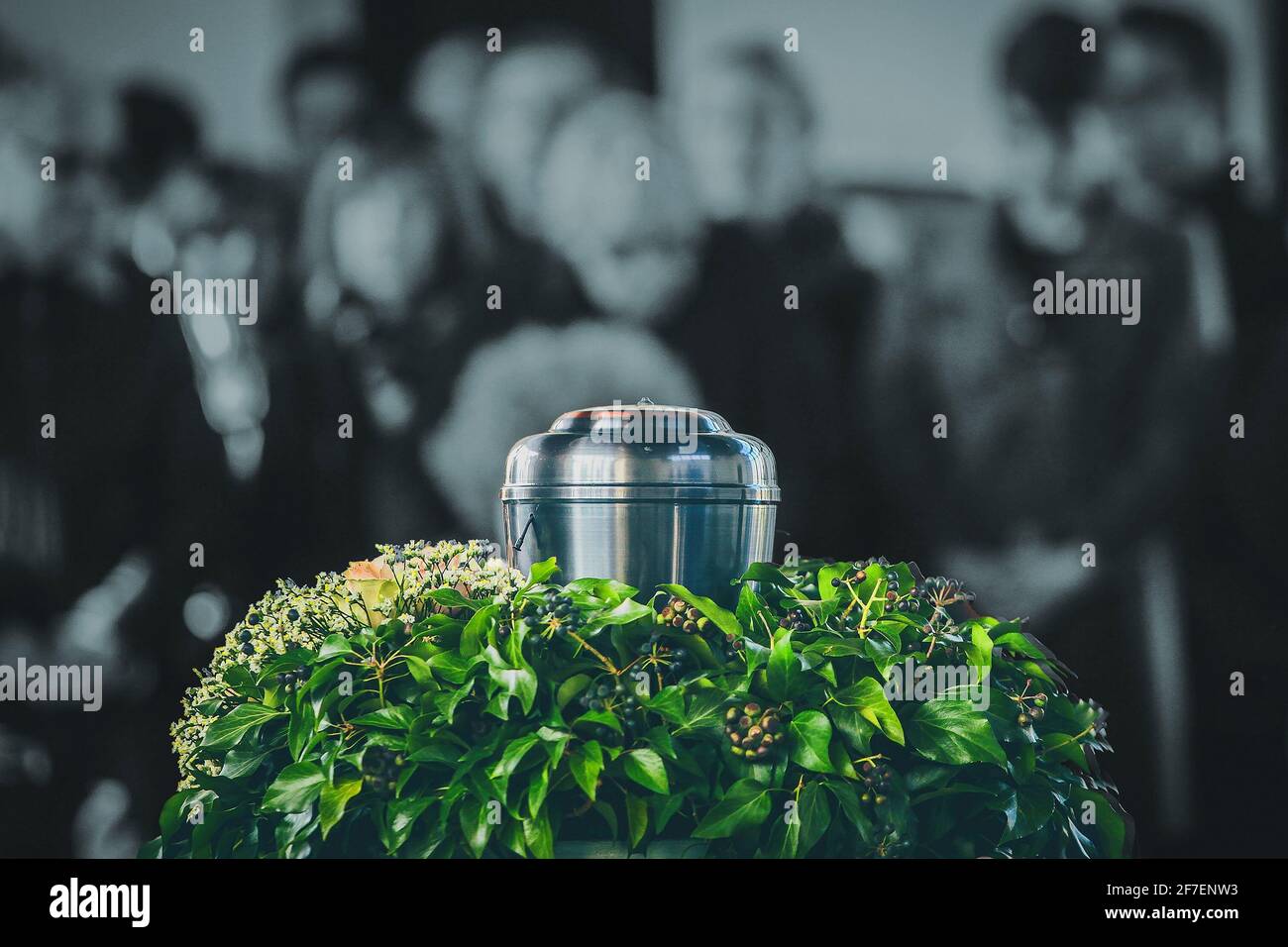 A metal urn with ashes of a dead person on a funeral, with people mourning in the background on a memorial service. Sad grieving moment at the end of Stock Photo