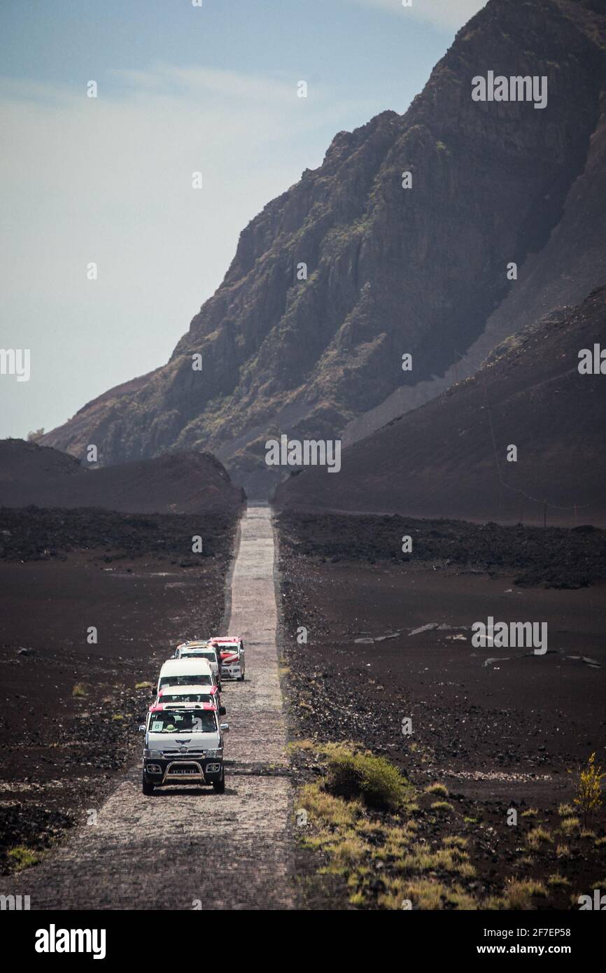 Cobblestone road with a caravan of cars and vans on it. Hills in the ...