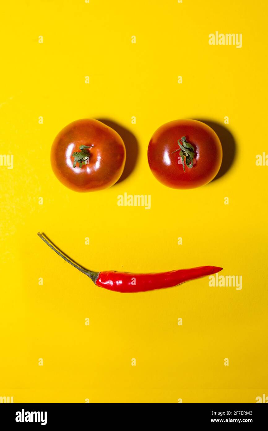face of tomatoes and hot peppers on a yellow background Stock Photo