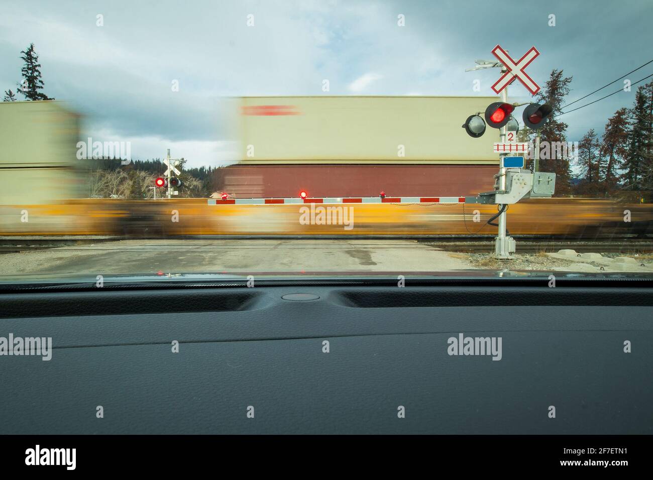 Grade crossing with heavy train loaded with containers in america. Train moving past the crossing in motion blur while lights are flashing Stock Photo