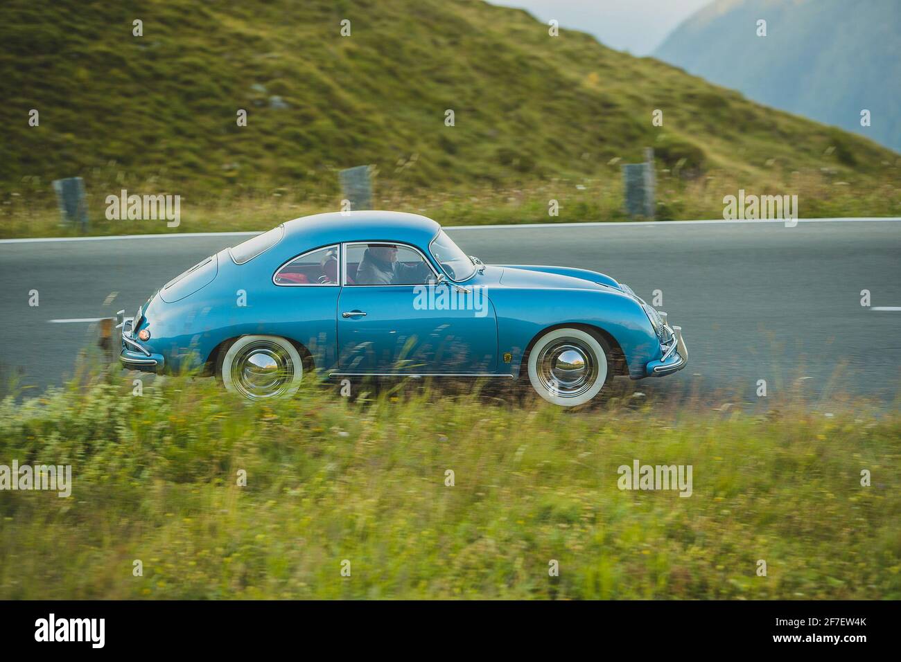 GROSSGLOCKNER, AUSTRIA, 17. AUGUST 2018: A vintage Porsche 356 sports car in blue color and whitewall tires is racing downhill over the pass of Grossg Stock Photo