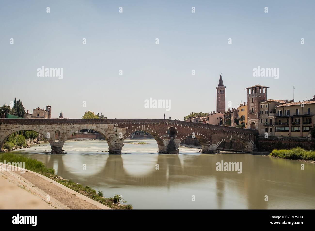 view of the famous Ponte Pietra in Verona, rising above the river of Adige in Italy. Long exposure daylight shot on a sunny day of an old brick bridge Stock Photo