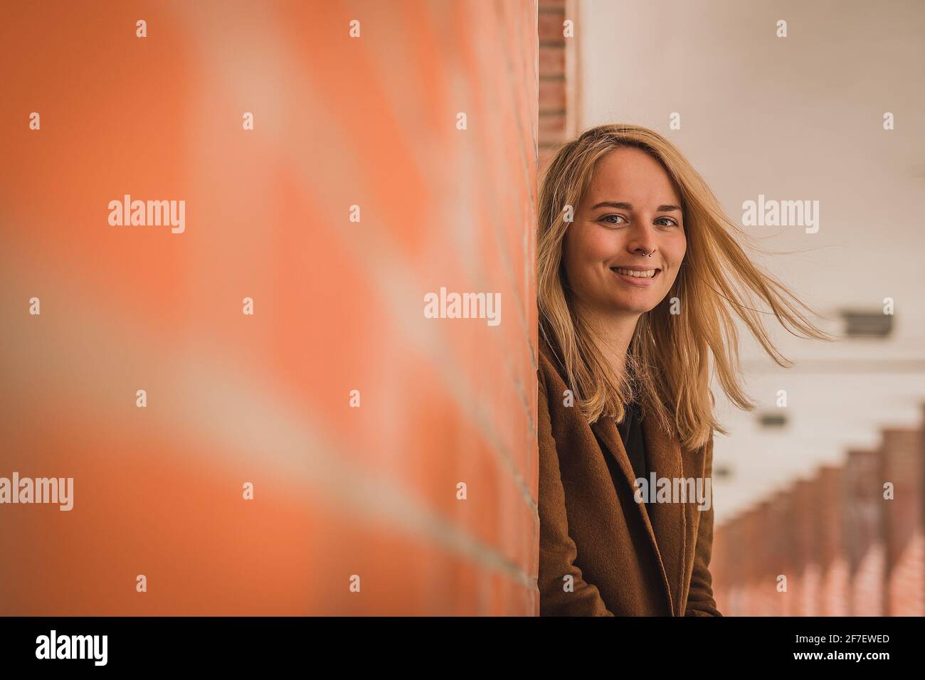 Cute fashionable young woman in a red brick hallway looking at a camera. Caucasian girl in a let's go mode, wanting to travel. Wanderlust hipster girl Stock Photo