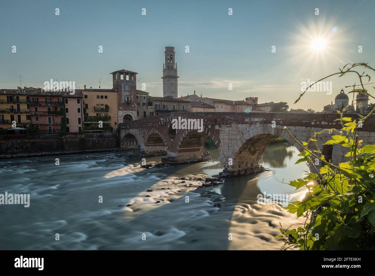 view of the famous Ponte Pietra in Verona, rising above the river of Adige in Italy on early afternoon. Long exposure daylight shot on a sunny evening Stock Photo