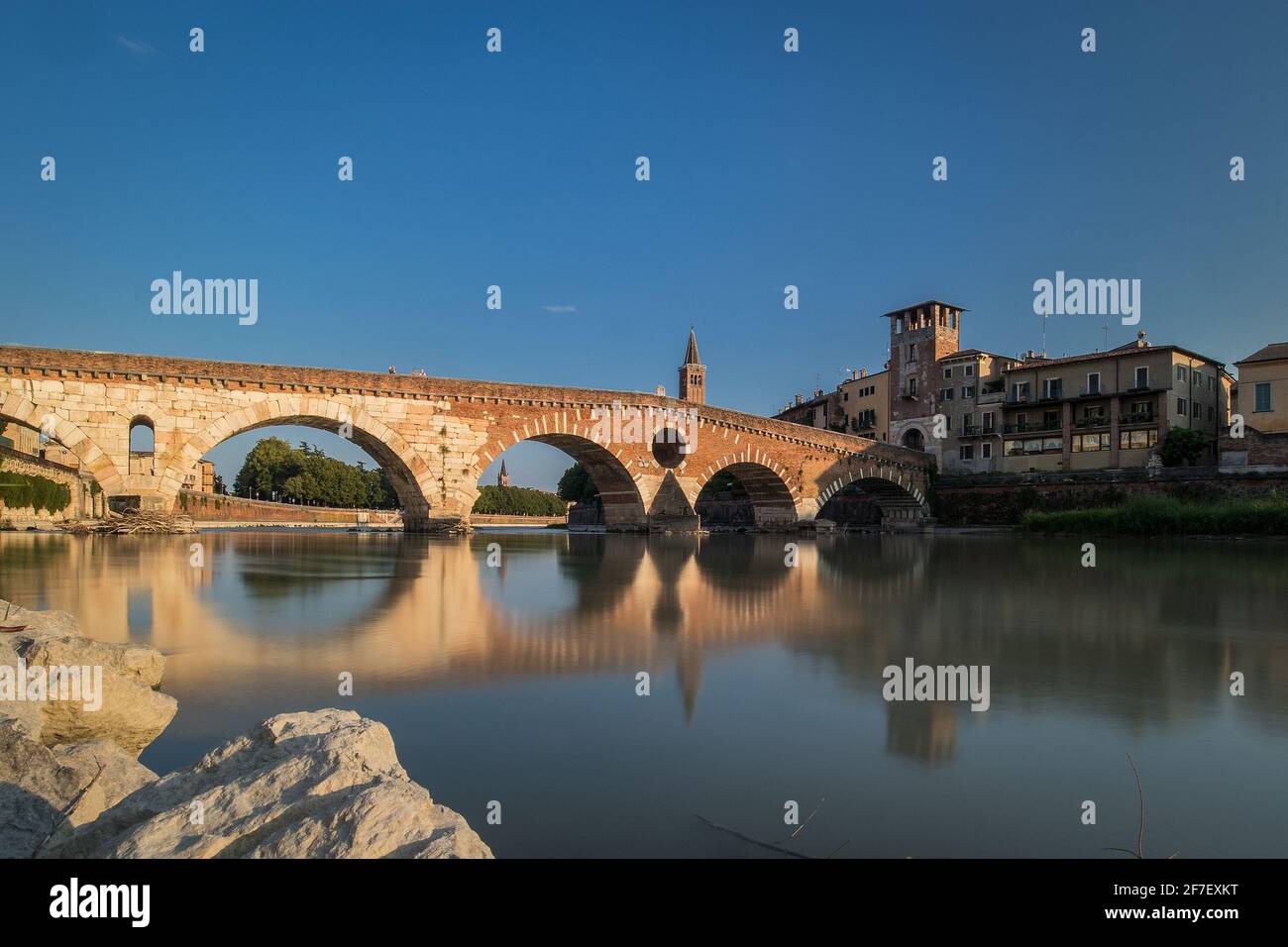 view of the famous Ponte Pietra in Verona, rising above the river of Adige in Italy on early afternoon. Long exposure daylight shot on a sunny evening Stock Photo