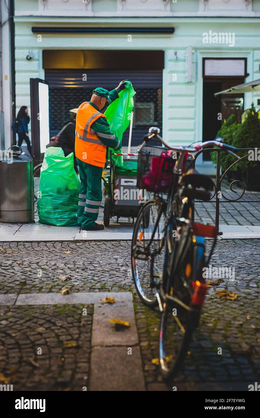 A worker is taking the trash out of the bin and into his cart. Protective clothing, bicycle in the foreground. Stock Photo