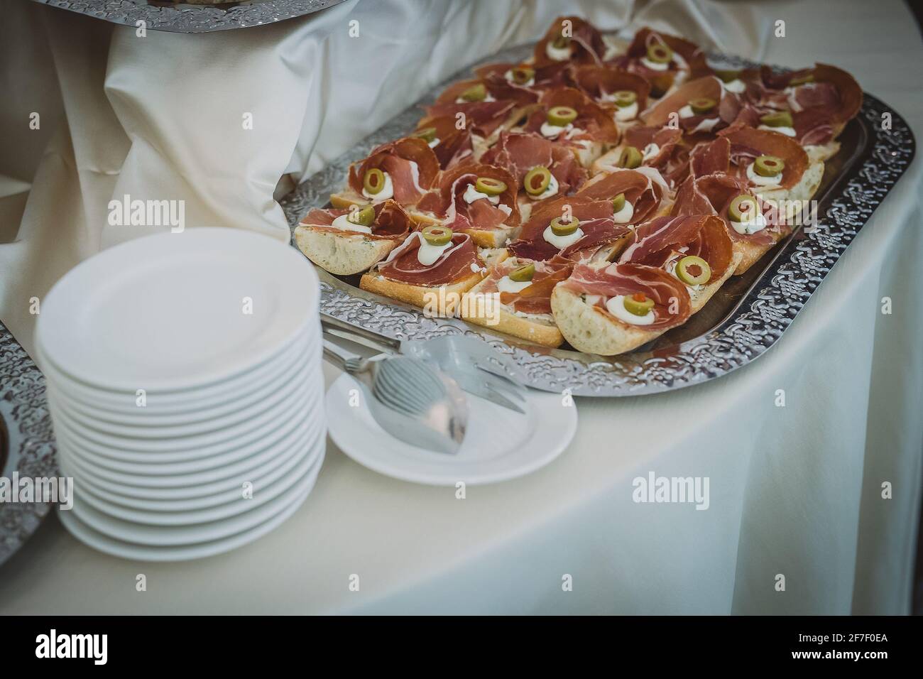 A collection of different snacks and sandwiches on a display on a silver plate at a gala event or a party. Hand is seen taking a prosciutto sandwich Stock Photo