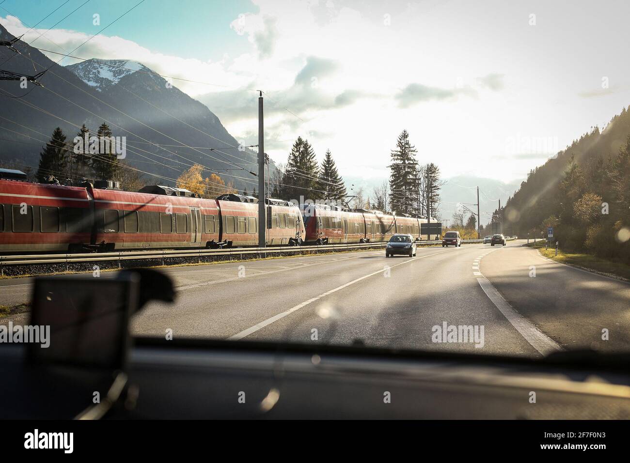 A commuter train in germany passing cars on a adjacent road. Concept of