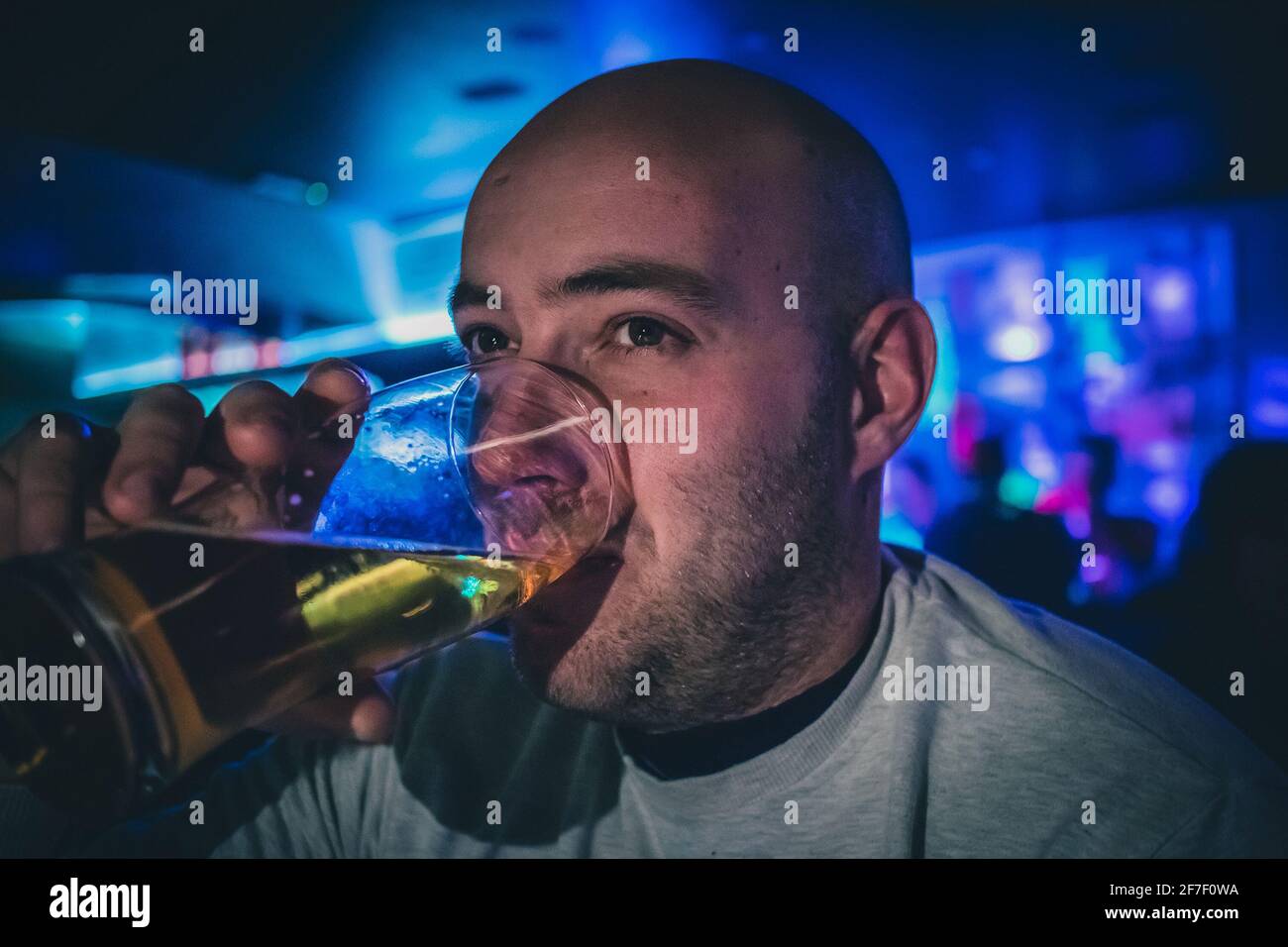 Young male drinking a pint of beer in a pary disco environment. One