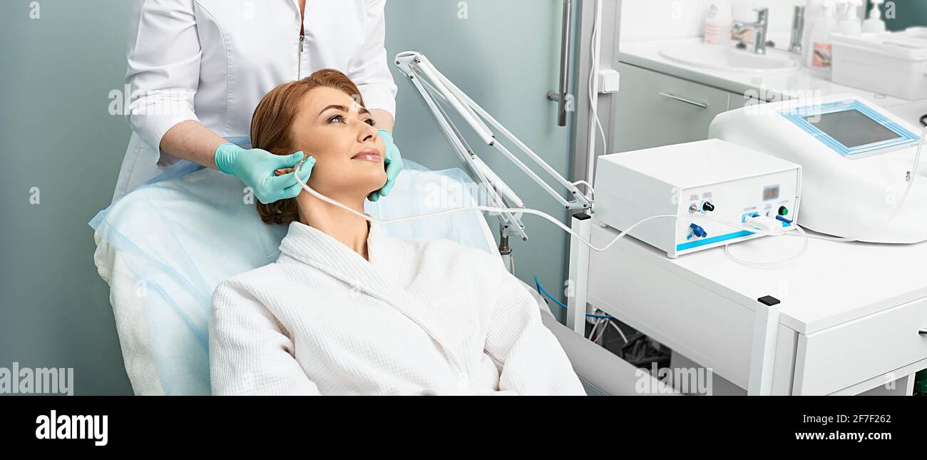 Adult woman getting rejuvenation skin face with ozone therapy procedure at beauty clinic using oxygen skin care machine Stock Photo