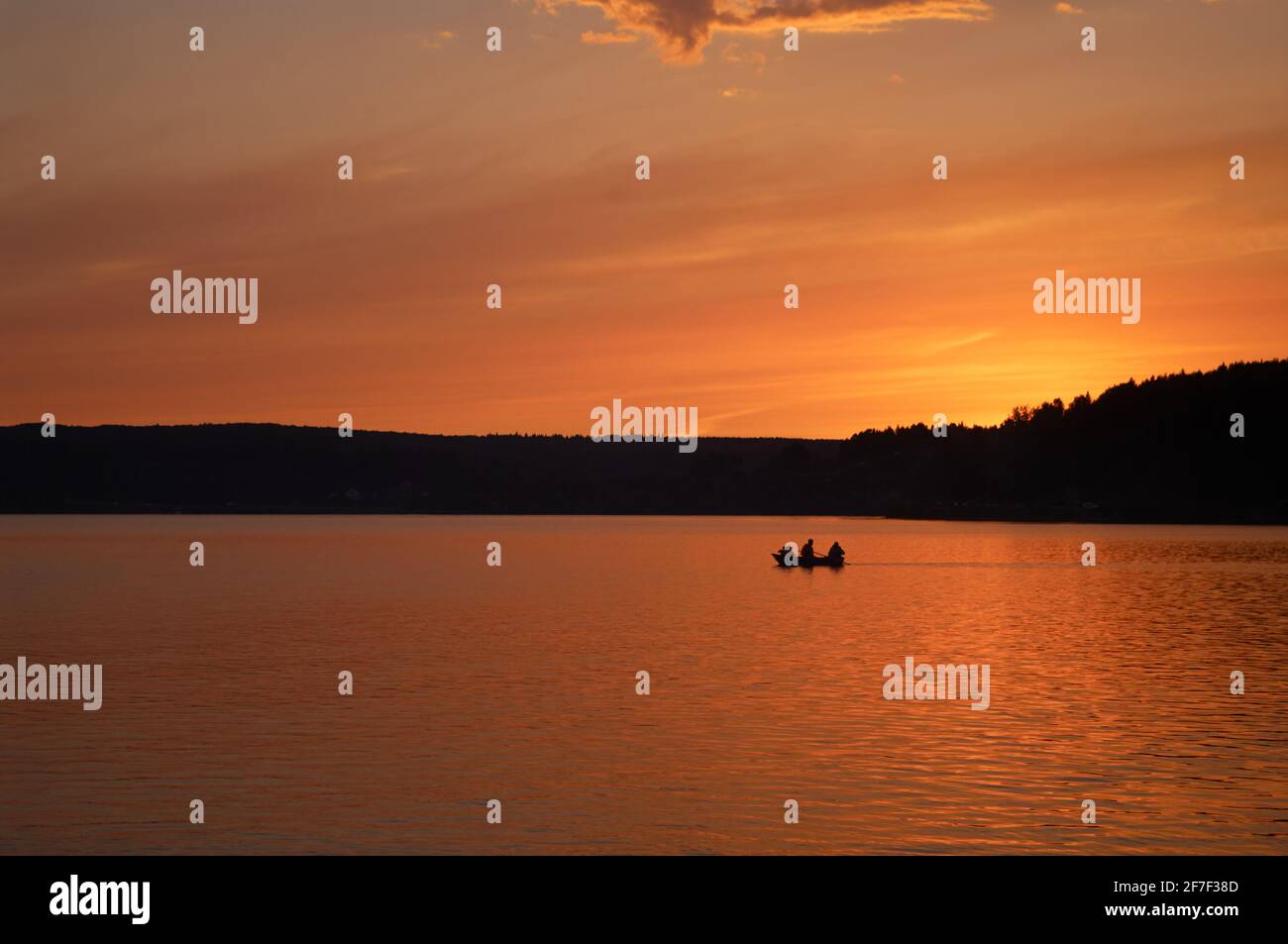 Rowboat with unrecognizable persons on water at sunset. Image of silhouette Stock Photo