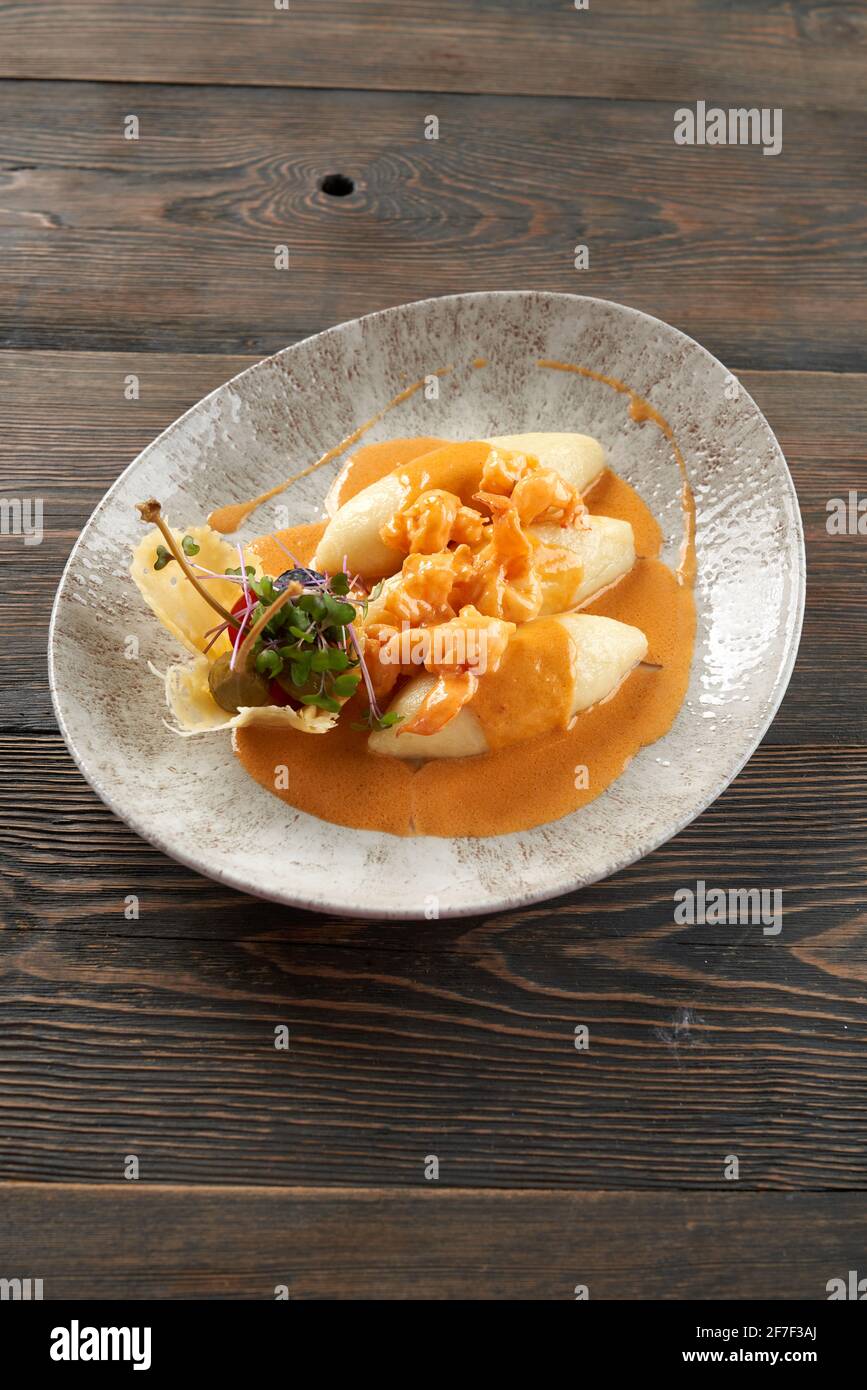 Delicious seafood with orange sauce on plate on table, three potato cutlets served with vegetables and sprouts in cheese basket. From above view of shrimps cooked in restaurant for dinner. Stock Photo