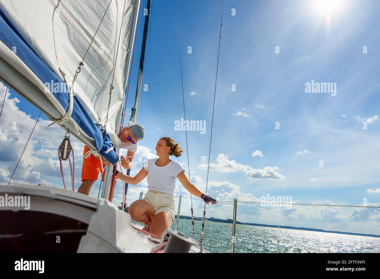 Young man and woman sailing on a yacht. Female sailboat crewmember trimming main sail during sail on vacation in summer season Stock Photo