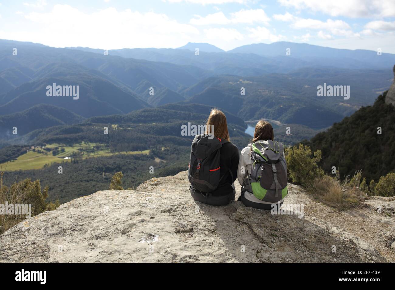 Back view portrait of two trekkers resting contemplating views on the top of a cliff in the mountain Stock Photo