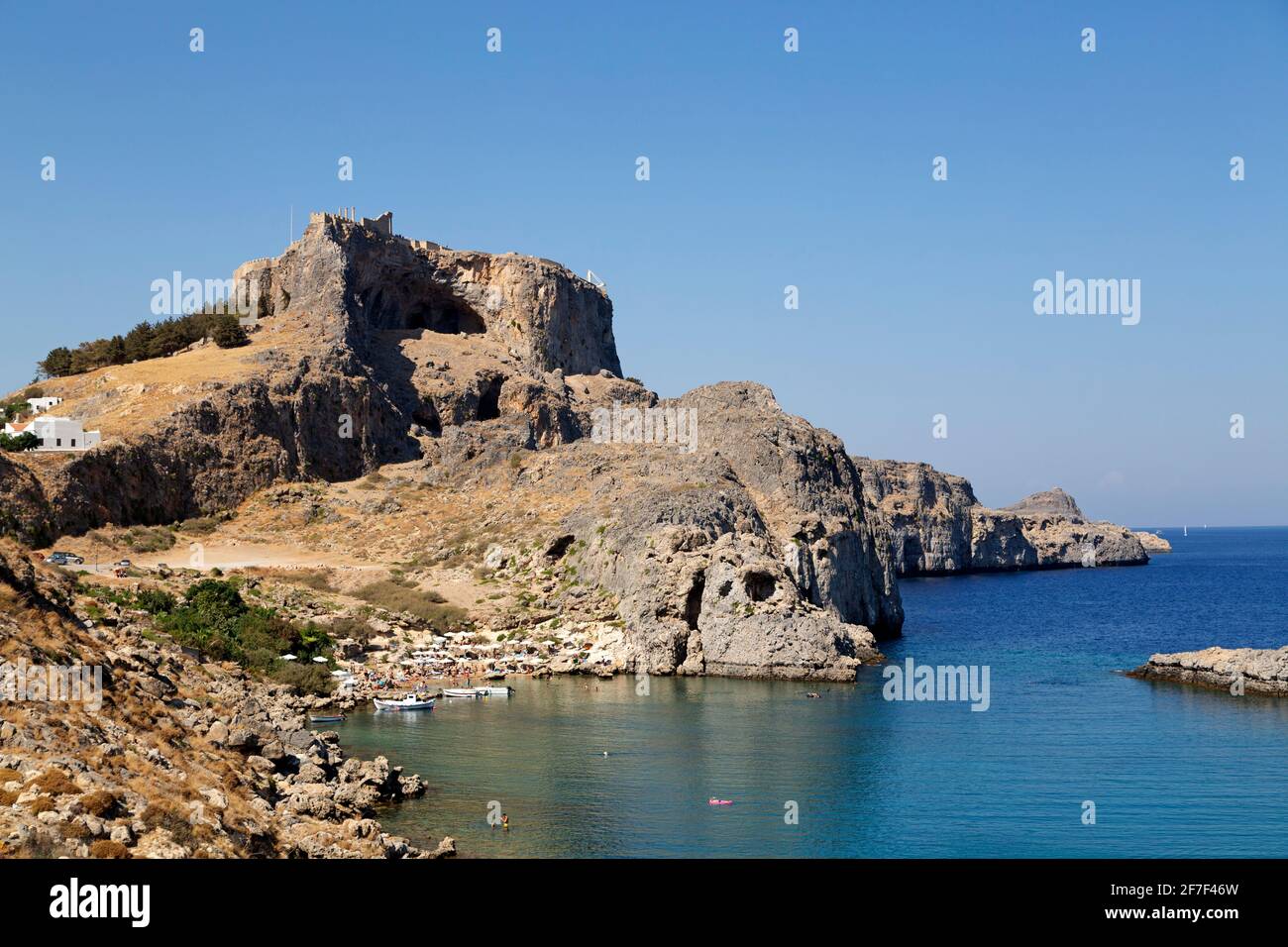 The Lindian Acropolis overlooks St Paul's Bay in Lindos on Rhodes, Greece. The ancient monument stands under a clear blue sky. Stock Photo