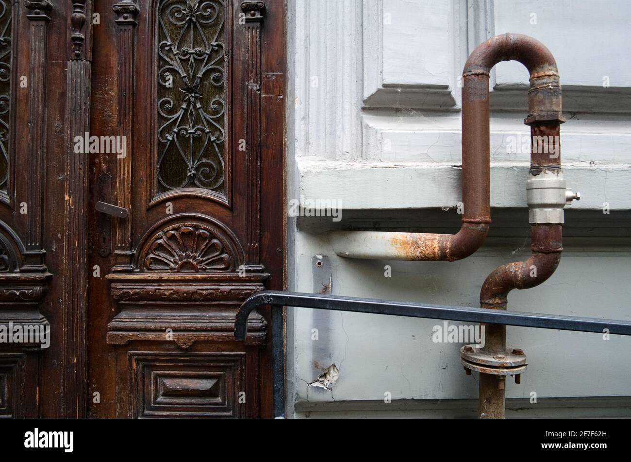 Old wooden vintage door and rusty gas pipeline on the wall outside on the street. Ivano-Frankivsk, Ukraine. Stock Photo