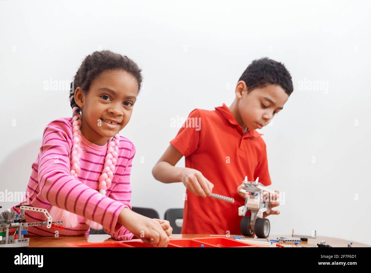 Front view of building kit for group of kids creating toys, having positive emotions and joy, selective focus of girl smiling and looking at camera. Close up of african friends working on project. Stock Photo