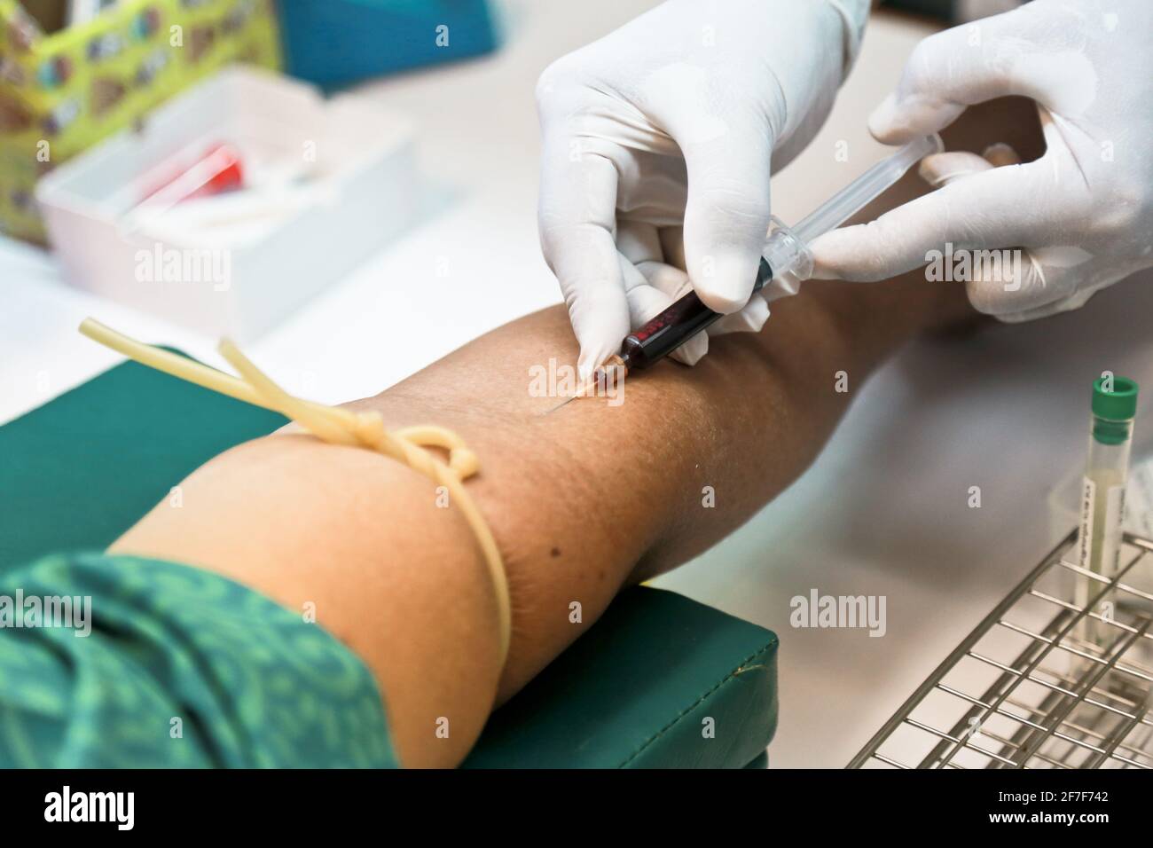 Doctor or nurse hands in medical white gloves using needle syringe drawing blood sample from patient arm in hospital. Stock Photo