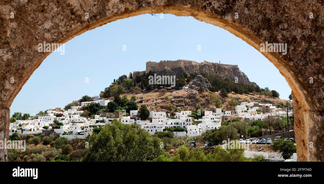 The Lindian Acropolis rises over white houses in the fishing village of Lindos on Rhodes, Greece. The Ancient Greek citadel and place of worship is se Stock Photo
