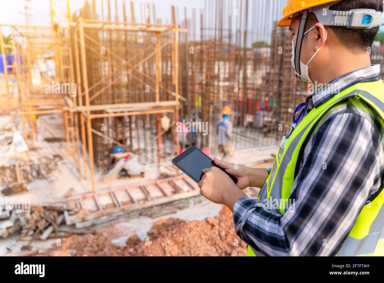 Construction civil engineer or architect with hardhat on construction site checking schedule and building foundations project on tablet computer at co Stock Photo