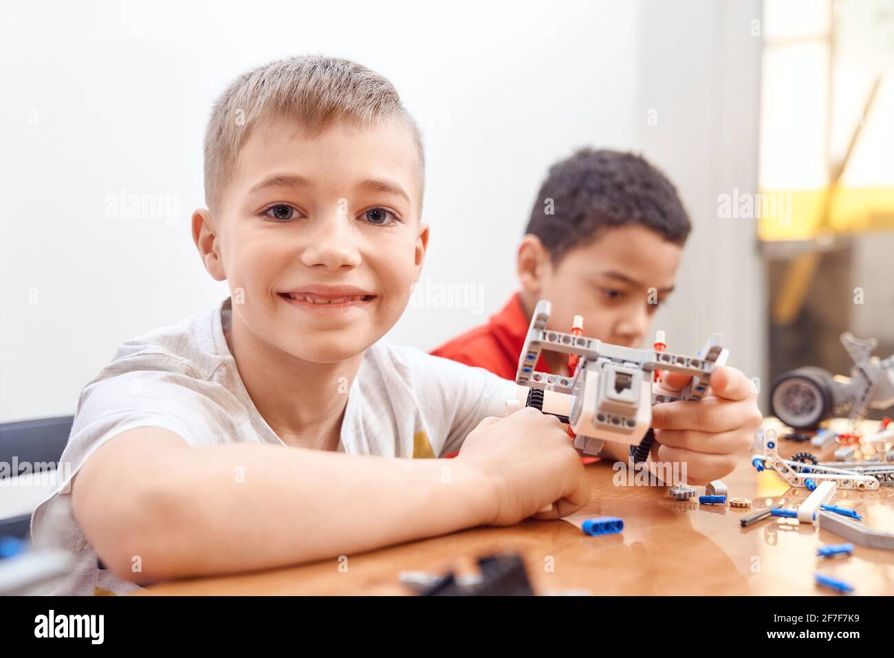 Side view of building kit for group of multiracial kids creating toys, having positive emotions and joy, lovely caucasian boy smiling and looking at camera. Close up of friends working on project. Stock Photo