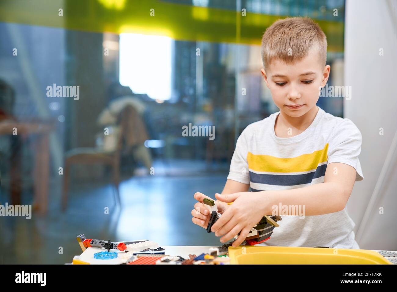 Selective focus of lovely caucasian boy working on project, taking colorful parts to create robot, having positive emotions and joy. Front view of building kit for kids. Science engineering. Stock Photo