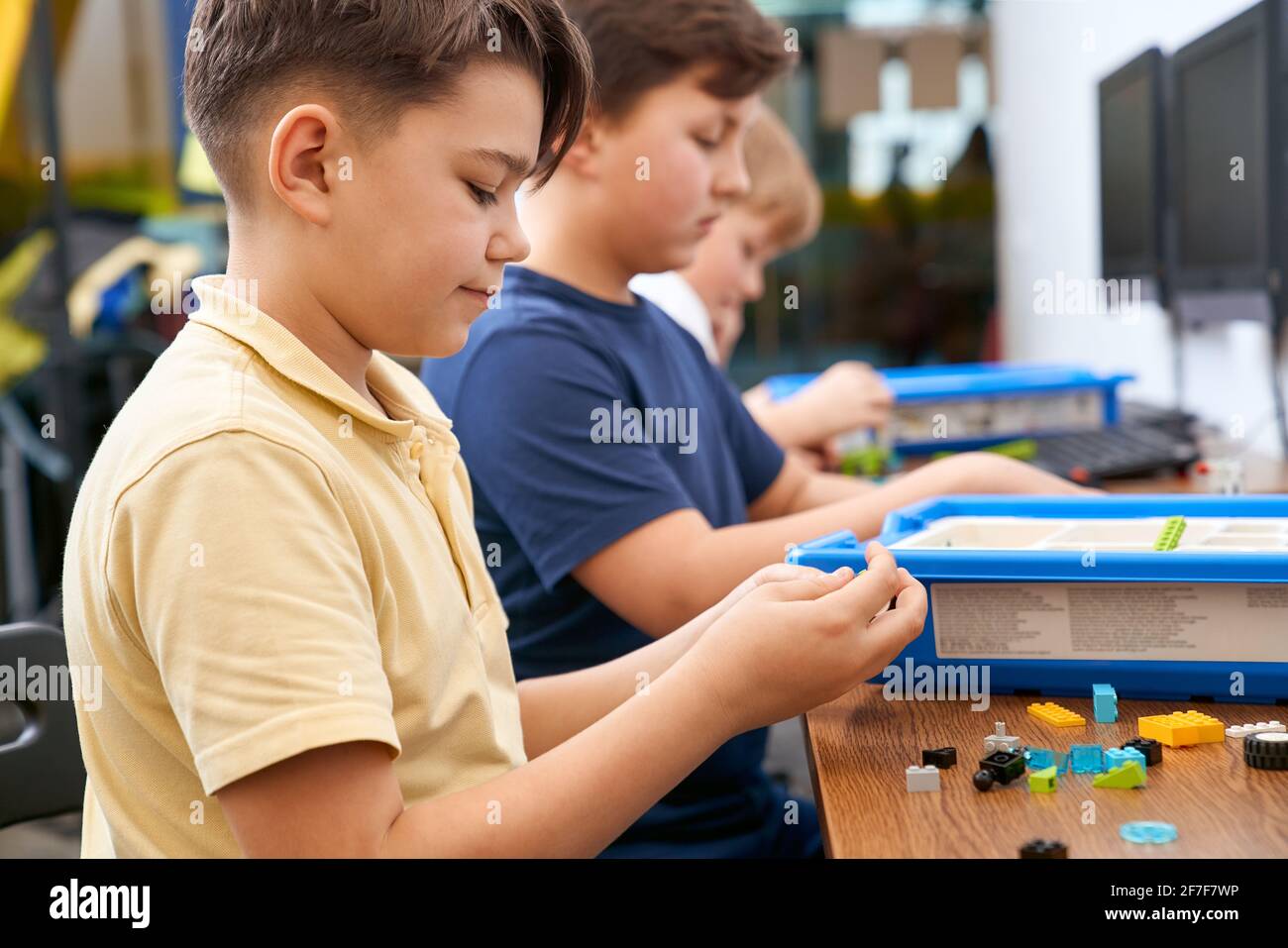 Interesting building kit for kids on table with computers. Side view of boys creating toys. Science engineering. Nice interested friends chatting and working on project together. Stock Photo