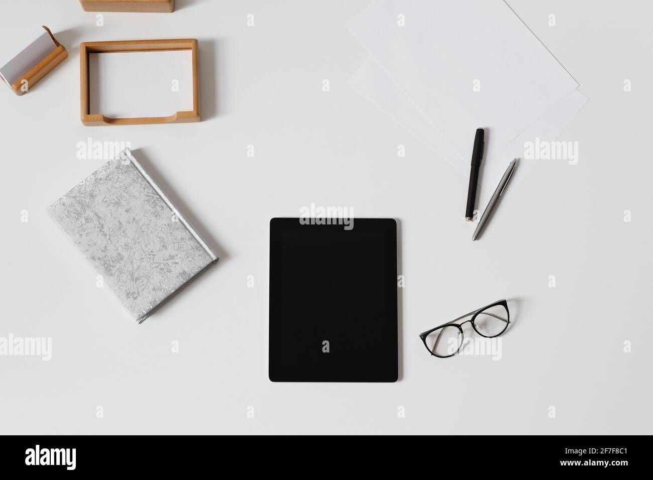 Flat lay of white desk table with a notepad, glasses, tablet, paper note, and pens Stock Photo