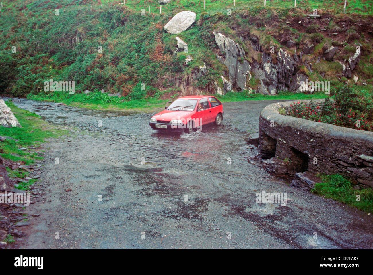 a car going through a stram that is flowing across a road, September 1990, Dingle Peninsula, Co. Kerry, Ireland Stock Photo