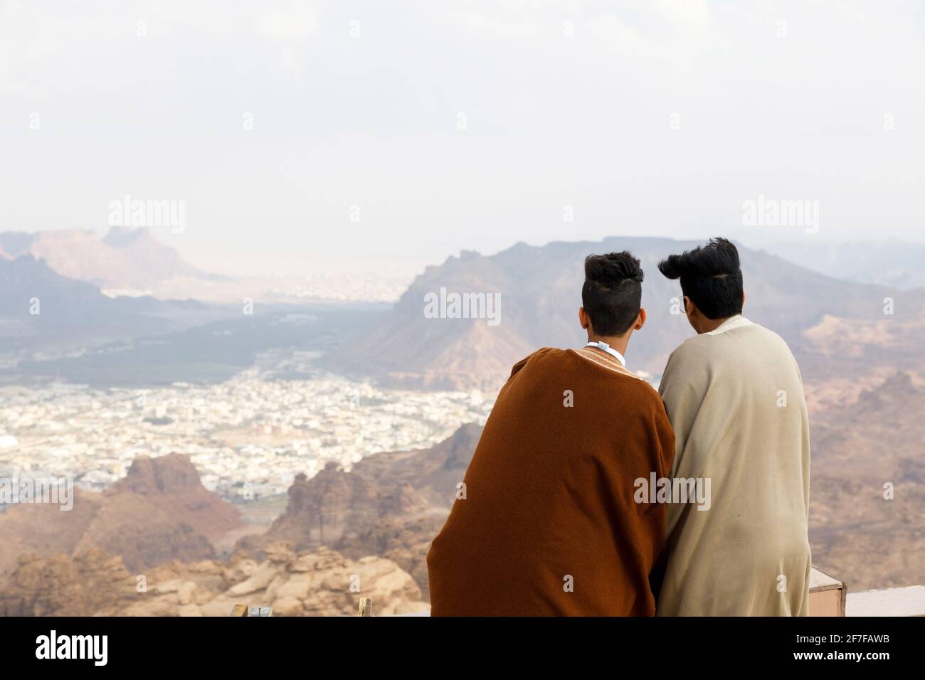 Al Ula, Saudi Arabia, February 19 2020: Two Saudi Arabian youths look from a viewpoint in the mountains towards the Al Ula oasis in Saudi Arabia Stock Photo