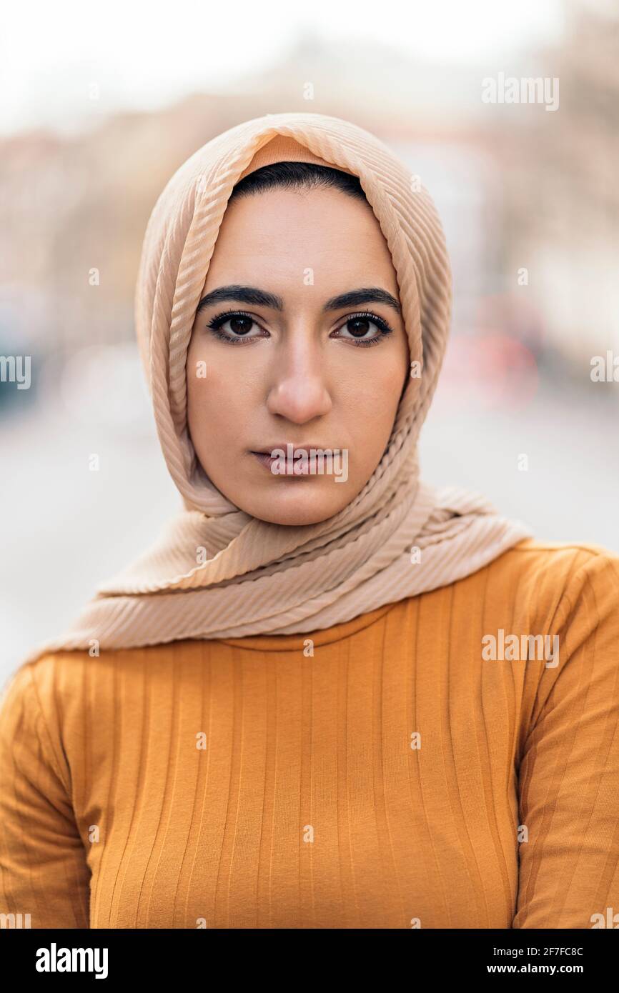 Expressive young muslim woman standing in the street wearing hijab and ...