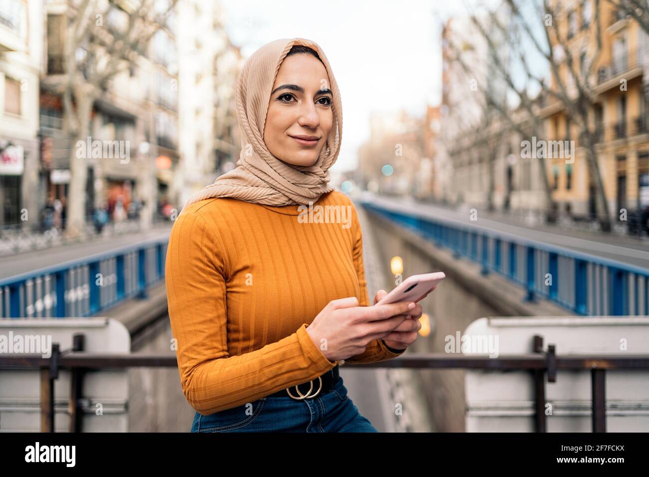 Pretty young muslim woman wearing head scarf using her mobile phone in ...