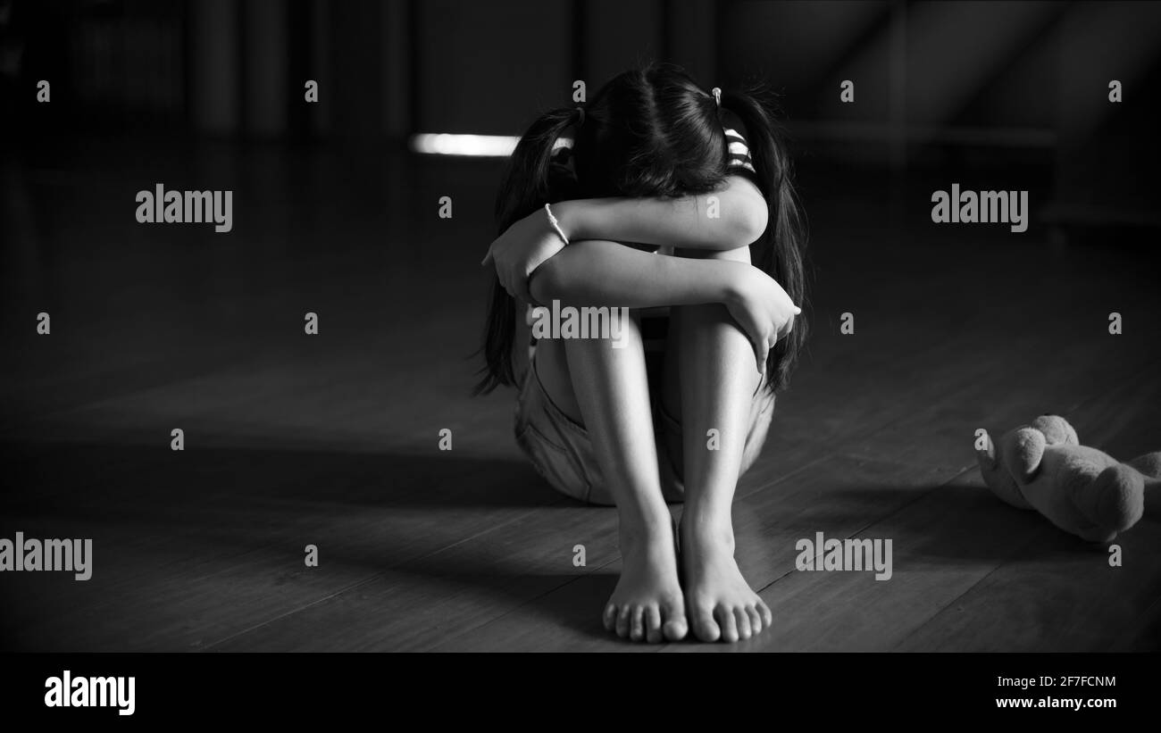 Alone little girl siting in the dark room with feel sad or cry.B&W and Low key style Stock Photo