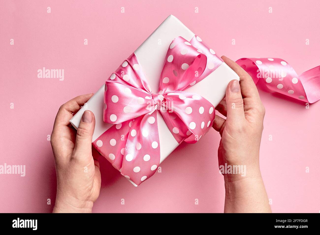 Gift box with big bow in female hands on pink background, top view ...