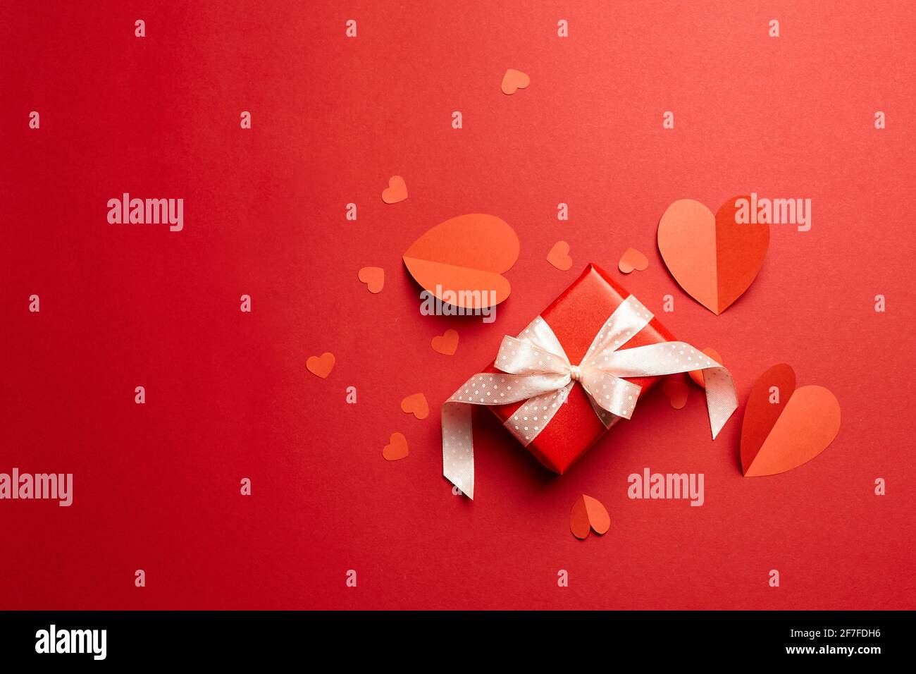 Gift box with bow and red paper hearts on red background, top view ...