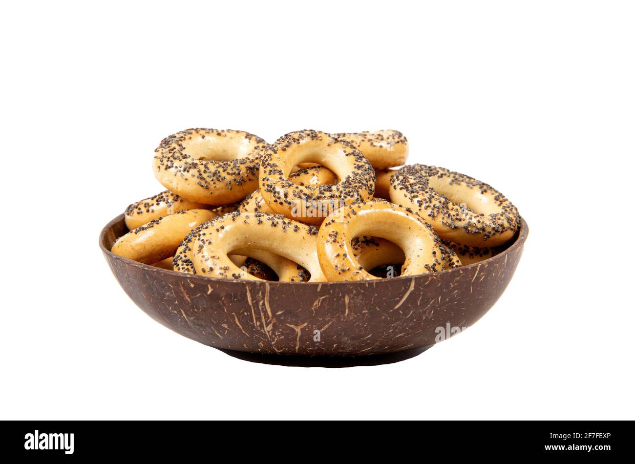Baranka sushka covered with poppy seeds. Eastern European salty cookie snack in brown natural coconut shell bowl, side view, isolated on white. Stock Photo