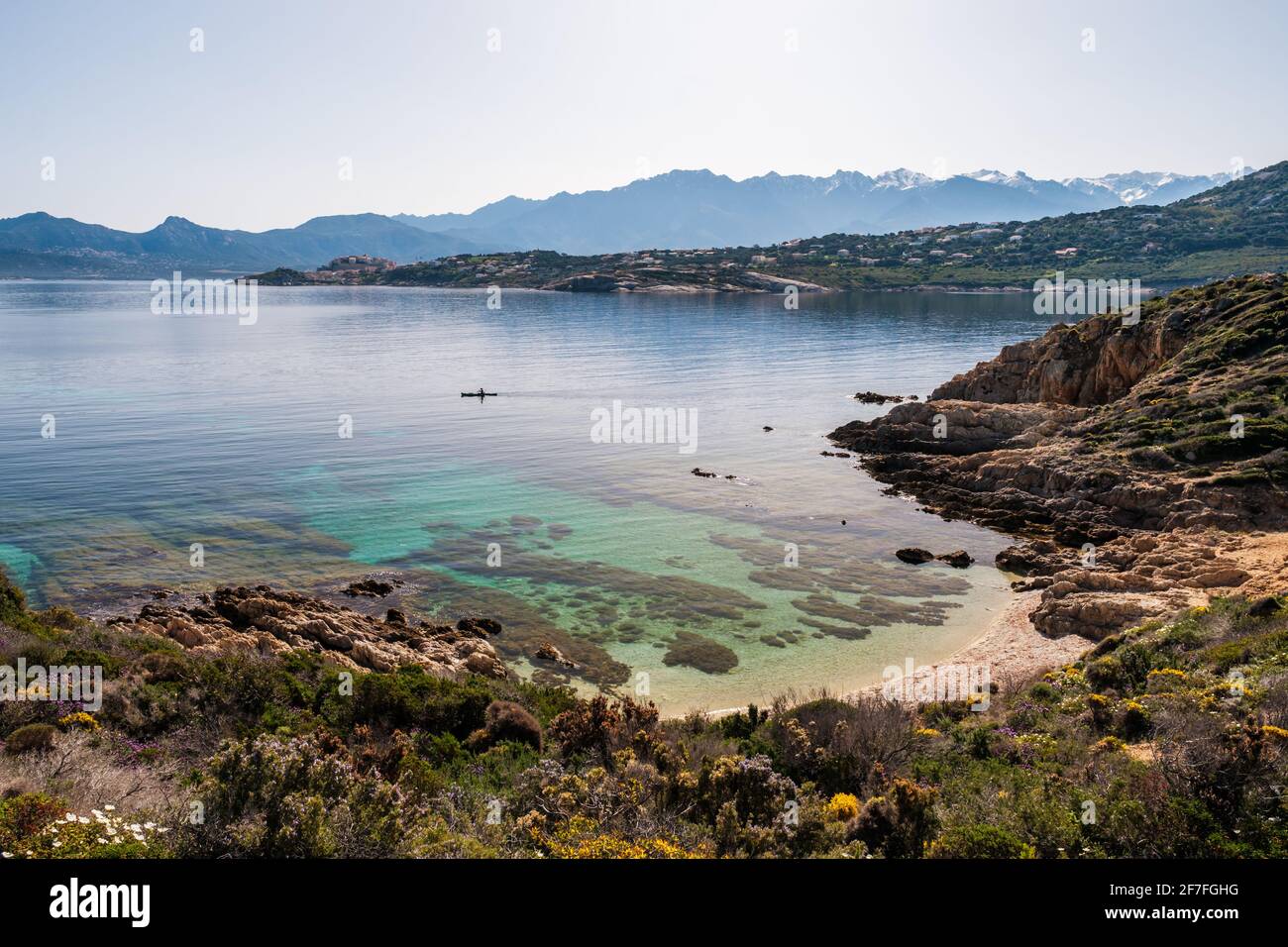A lone kayaker paddles across a small shallow cove on the translucent Mediterranean sea on the coast of La Revellata in the Balagne region of Corsica Stock Photo