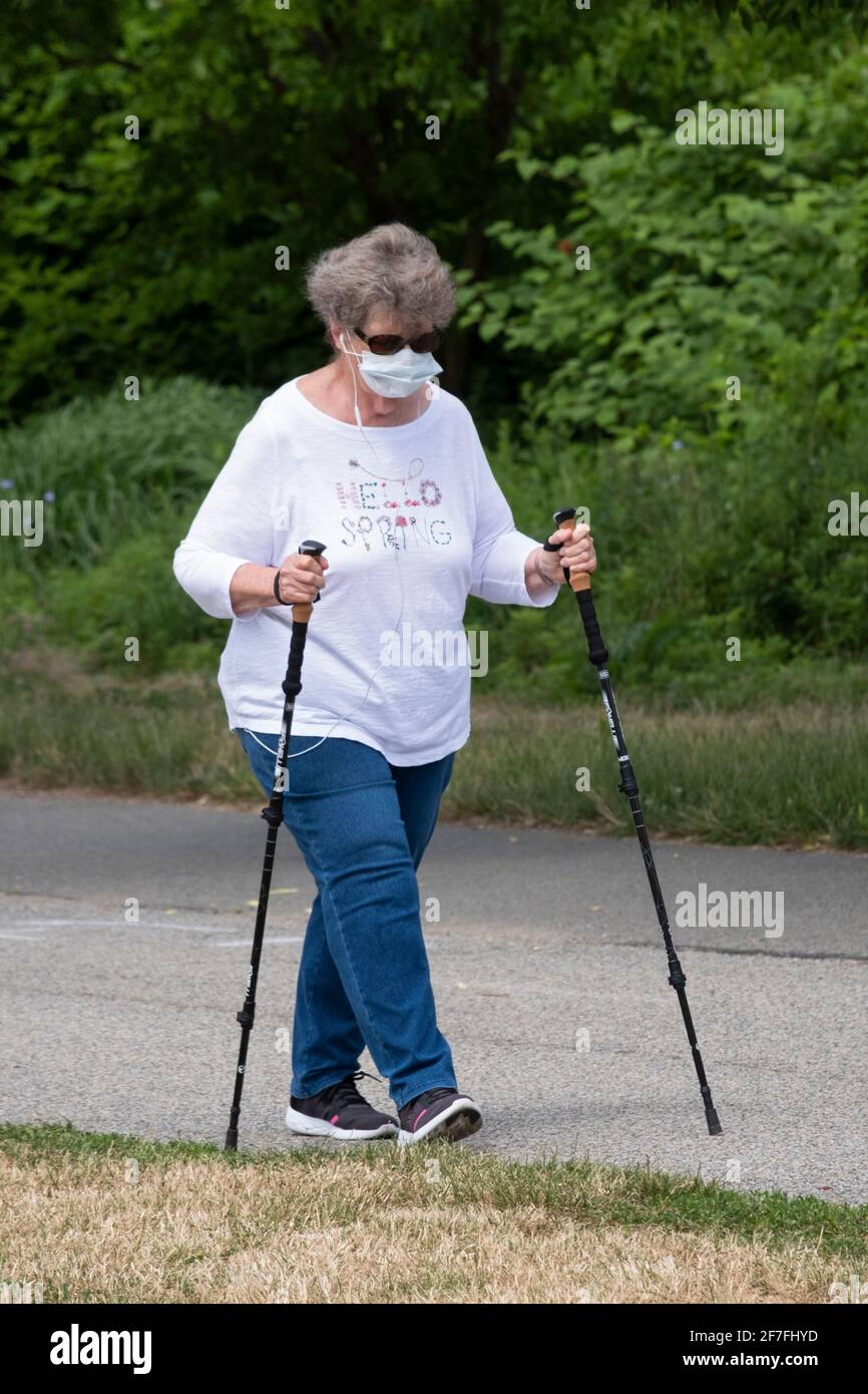 An older woman out for an exercise walk in Little Bay Park in Whitestone, Queens, New York using walking sticks and listening to music. Stock Photo