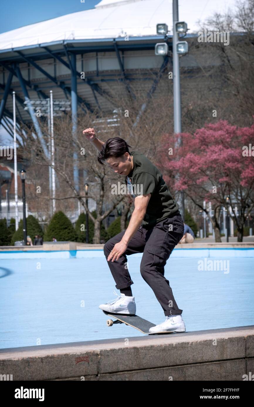 An Asian American skateboarder does a trick of sliding his board along a thin concrete embankment near the Unisphere in Flushing Meadows Corona Park. Stock Photo