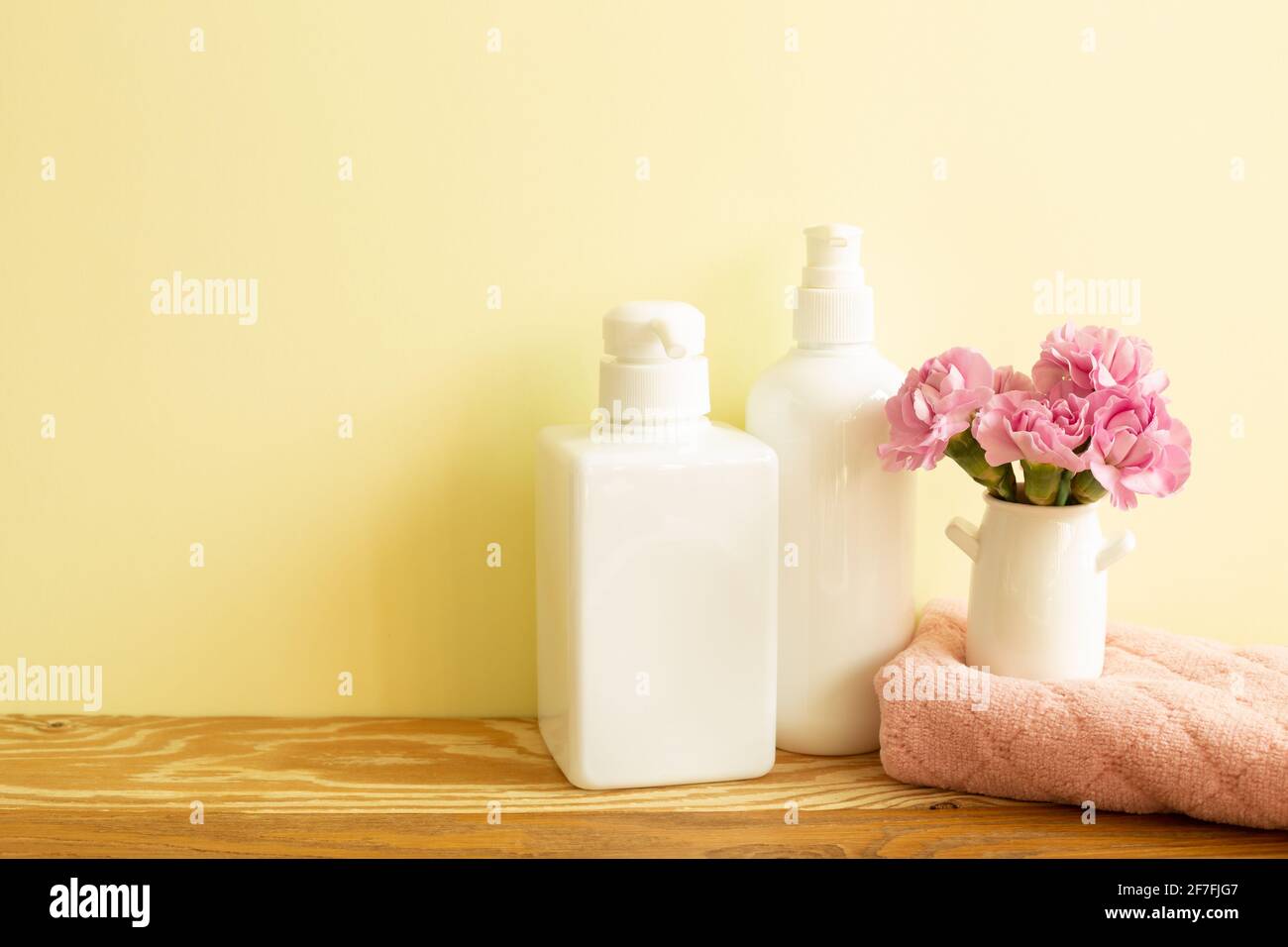 Skin care and spa concept. Bathroom bottles and towel with pink flowers on wooden shelf. yellow background Stock Photo