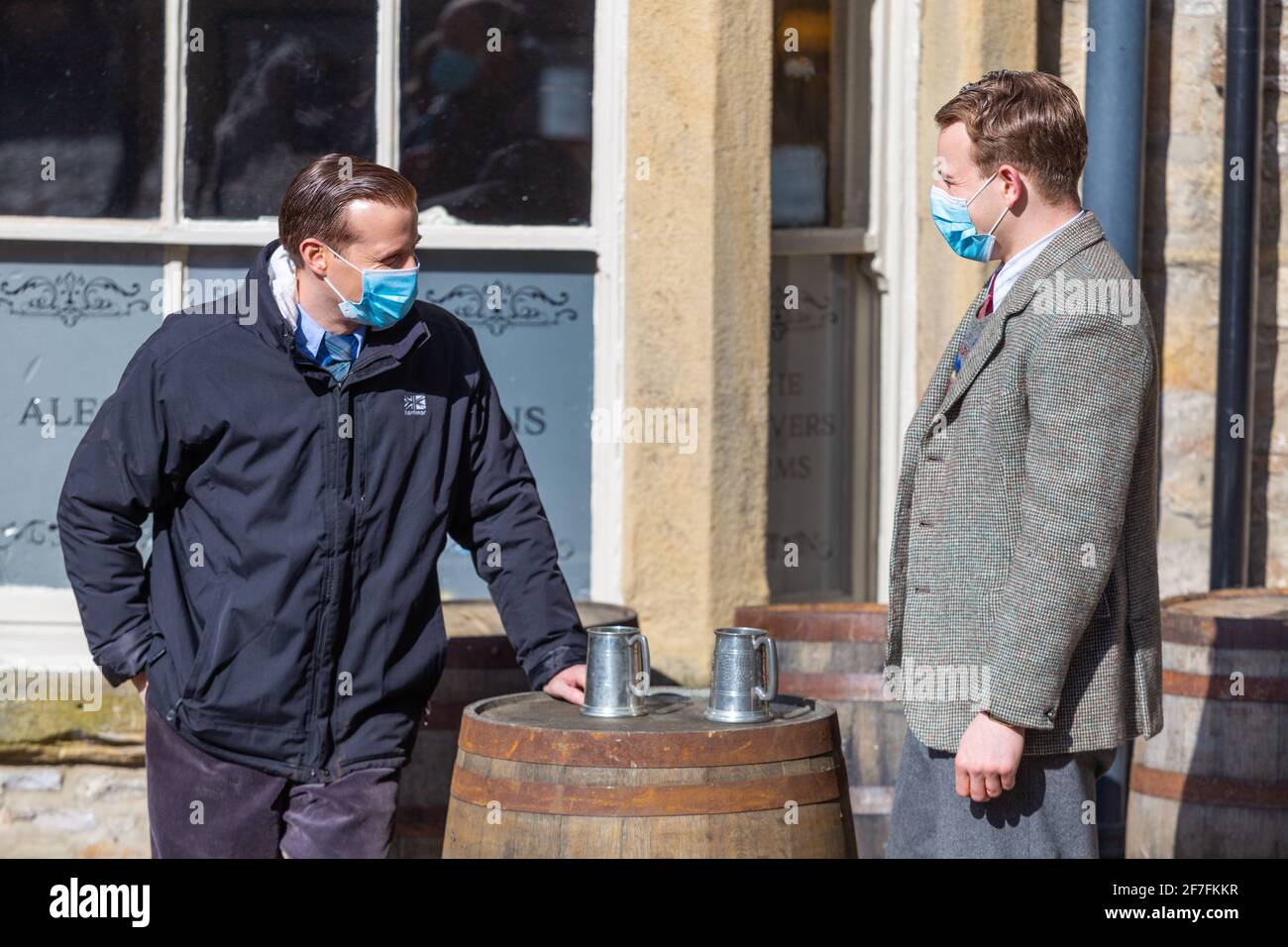 Grassington, UK. 7th April 2021. Nicholas Ralph (James Herriot) and Callum Woodhouse (Tristan Farnon) rehearse a scene wearing masks during filming for the second series of the Channel 5 re-make of All Creatures Great and Small takes place in village of Grassington in the Yorkshire Dales Nation Park. (Credit: Tom Holmes Photography / Alamy Live News) Stock Photo
