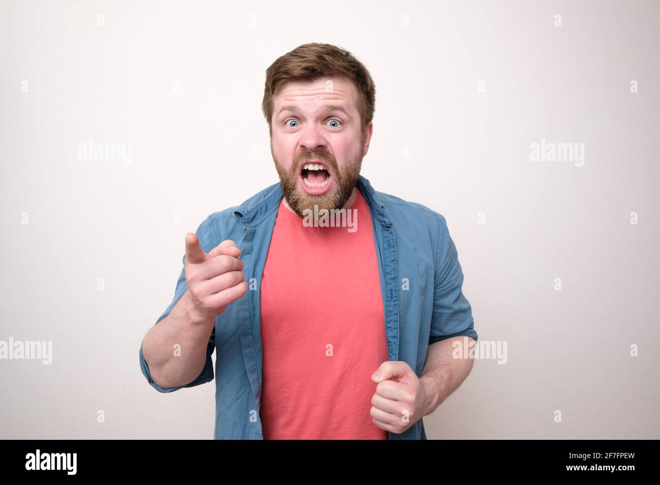 Aggressive bearded man yells and reproaches someone, he looks viciously, points his finger and blames. White background. Stock Photo