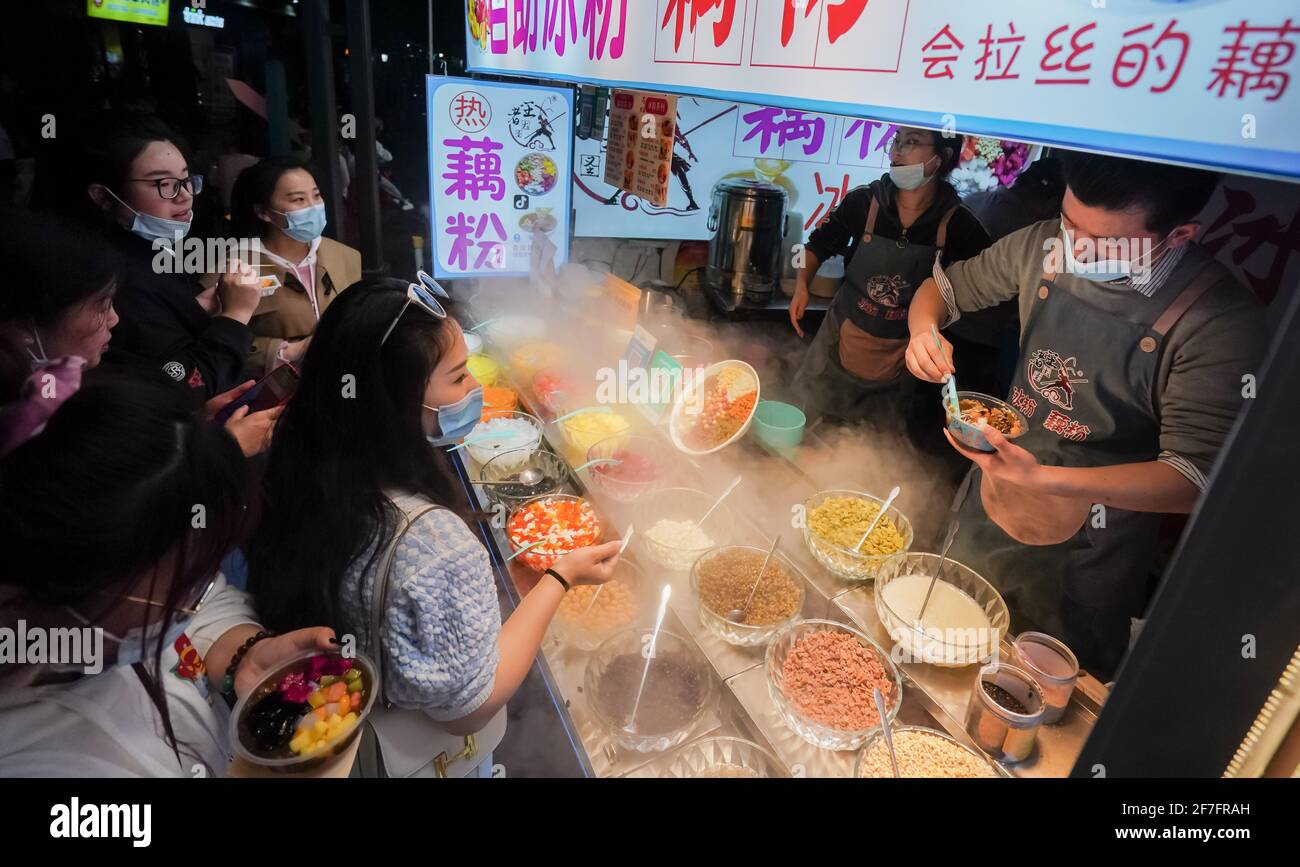 Wuhan, COVID-19. 8th Apr, 2020. People eat snacks at an alley in Wuhan, central China's Hubei Province, March 28, 2021. Wuhan, once hit hard by COVID-19, has seen its urban life at night return to normal since its lockdown was lifted on April 8, 2020. Credit: Cheng Min/Xinhua/Alamy Live News Stock Photo