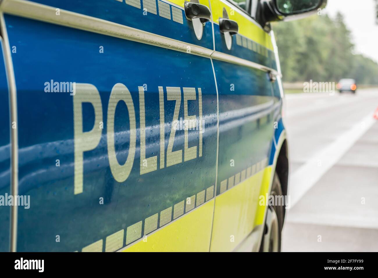 side view of a German police car on the autobahn. Lettering with reflective stripes on the body on a blue and yellow background. Rainy lanes and trees Stock Photo