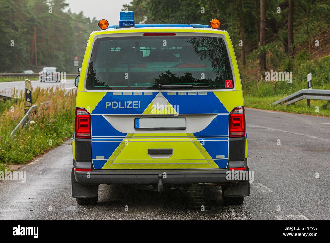 Rear view of a radio patrol car from the Brandenburg motorway in an emergency stopping bay. Police car in yellow and blue paintwork on a wet road. Stock Photo